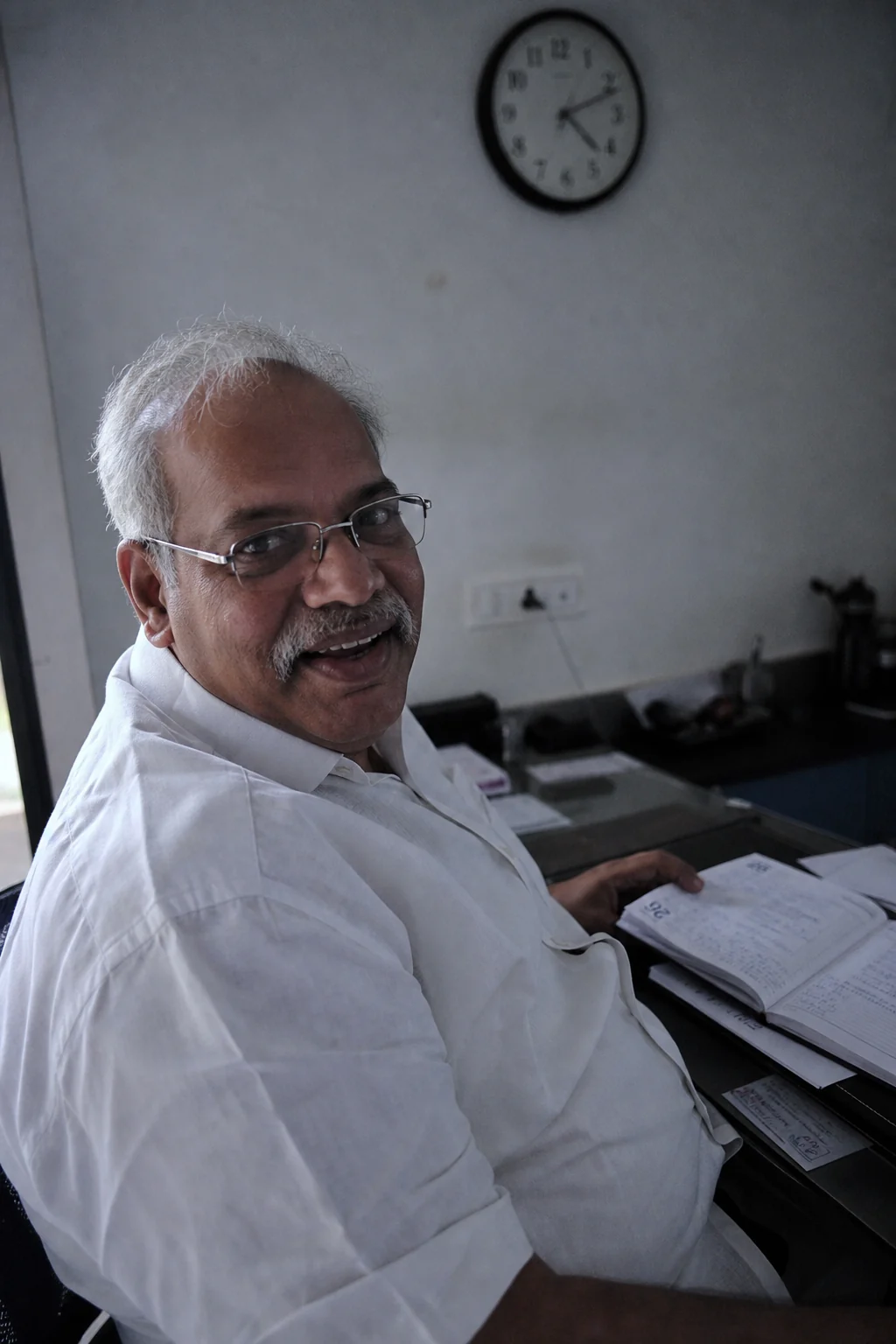 Ramesh Vemula turned in his chair at the clinic front desk with an appointment diary open, smiling at the camera.