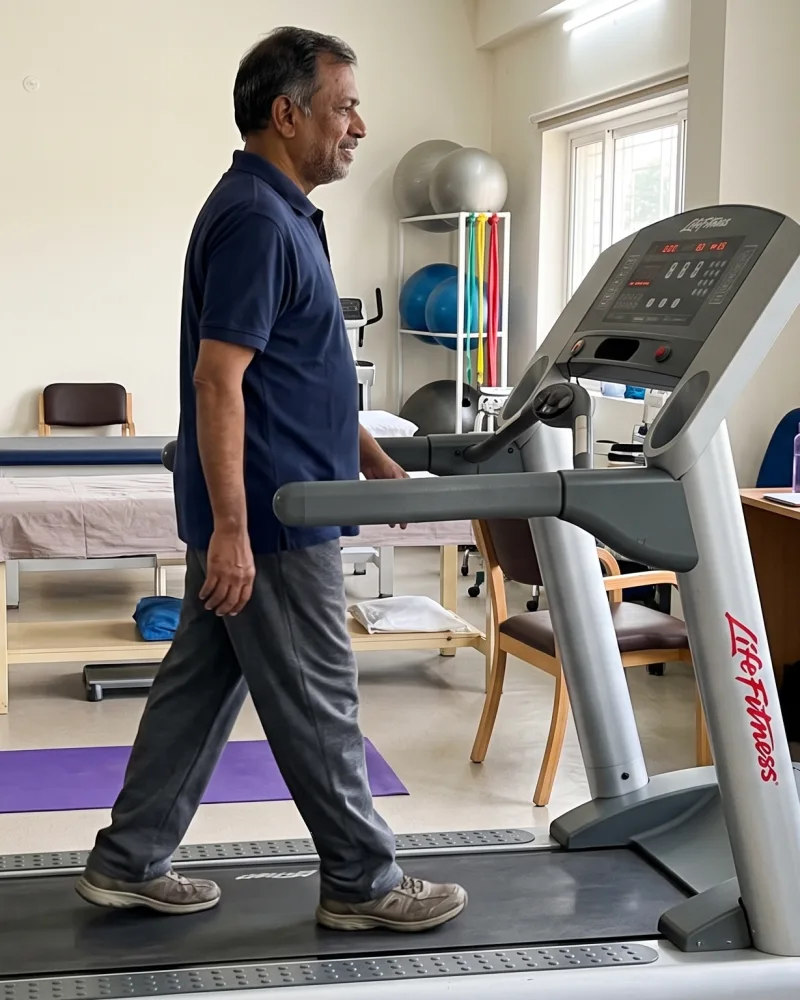 A man walking a treadmill in the clinic gym, watching the console ahead of him.